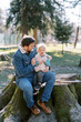 © VolodymyrNadtochii - Smiling dad with a laughing little girl on his knees sits on a huge stump in a sunny meadow