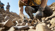 © Chineewan Somsap - Man digging rocky soil, focused uncovering fossils or artifacts, surrounded by nature and fellow diggers, showcasing determination and teamwork