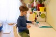 © Ivan Traimak - Young boy studying at a desk in a colorful room during afternoon light, engaged in learning with worksheets