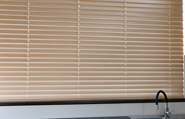 Fototapete - A wide view of closed beige wooden venetian blinds covering a large window above a kitchen sink. Automatic wood blinds in the kitchen are all about convenience and comfort.