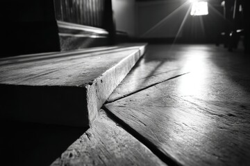 Poster - Monochromatic view of wooden floor and steps with sunlight streaming through window, creating contrast and highlighting textures in the interior space.