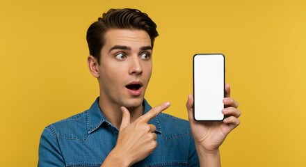 Poster - Man showing smartphone with blank screen looking surprised on yellow background. Man pointing finger at phone in hand with open mouth and raised eyebrows