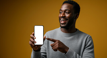Poster - Happy man pointing finger at smartphone with white screen display in hand against yellow background. Man showing mobile phone with empty screen for mockup