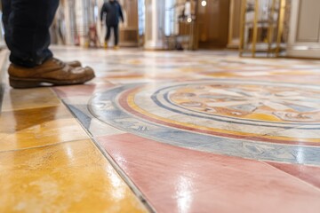 Poster - An elaborate tiled floor with intricate designs and a person standing on it, captured from a low-angle perspective, emphasizing detail and artistry.