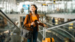 © Chanakon - happy young asian woman traveler holding boarding pass ticket, passport and smartphone at the airport terminal with her luggage and smiling at camera, cheerful tourist female having holiday trip.