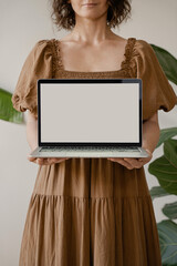 Wall Mural - Woman Wearing Earthy-Toned Dress Displaying Blank Laptop Screen, Soft Light and Natural Aesthetic