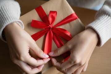 Aufkleber -  A person's hands holding a brown gift box with a red ribbon on it.