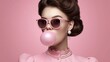 © NovaVision - A fashionable woman with pink sunglasses blows a bubblegum bubble against a pink background.
