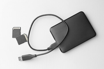 Poster - External hard drive with USB cable and SD memory cards on white background, flat lay