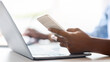 © Prostock-studio - Unrecognizable black woman using smartphone and working on laptop in white office, checking new mobile app, messaging on cellphone, browsing online banking, cropped image with selective focus
