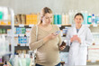 © JackF - Pregnant woman in pharmacy scans QR code on medicine syrup product, checks certificate on manufacturers website. Girl pharmacist offer similar product in background.