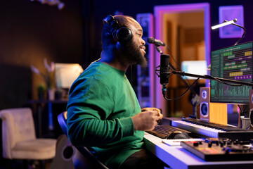 Fototapete - Young producer performing a live acoustic song in home studio, recording a new track on microphone and using DAW software. Artist songwriter editing the audio files in post production.