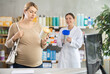 © JackF - In sales area of drug store, pregnant woman examines formula for feeding packaging, buys product. Girl pharmacist in background offers similar product, promotes product of European brand.