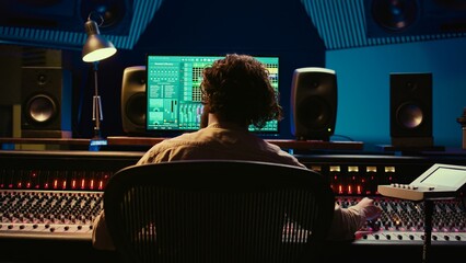 Poster - Audio technician working in control room to edit and process tracks, using audio software on pc for music industry post production. Skilled producer creating tunes with mixing console. Camera B.