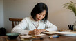 © Postmodern Studio - Asian mature female writing at home desk with concentration and creativity