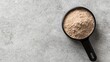 © MOPP - A close-up of a black measuring cup filled with light brown powder on a textured gray surface, suggesting culinary or nutritional use.
