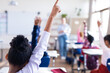 © WavebreakMediaMicro - In school, diverse students raising hands in classroom, engaging with female teacher