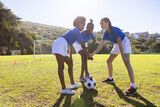 Playing soccer, three school diverse girls in sports uniforms strategizing on field