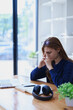 © Jirapong - Stressed young woman overwhelmed by e-learning studies at desk with laptop, notebook, headphones, hands clasped to her face in frustration