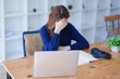 © Jirapong - Stressed young woman overwhelmed by e-learning studies at desk with laptop, notebook, headphones, hands clasped to her face in frustration