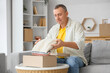 © Pixel-Shot - Mature man unpacking box with sweater at home