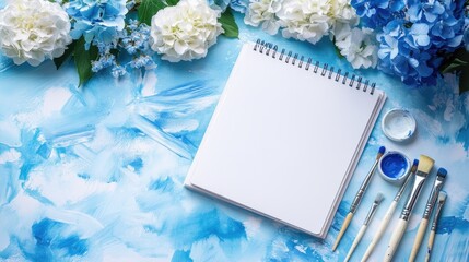 Aufkleber - An open sketchbook on a soft blue watercolor backdrop, with brushes, paints, and white and blue flowers, suggesting the creative flow of artistic endeavor.