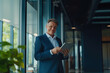 © PRASANNAPIX - middle age businessman standing confidently holding tablet in hand