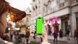 © VAKSMANV - Side view of Caucasian female with red hair holding smartphone with one hand. Mobile device with green screen. Chroma key visible on display. Girl looking with focus at display without touching.