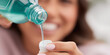 © Inspire Shots Hub - Close-up of teal mouthwash pouring into a cap, blurred woman smiling in background, showcasing oral hygiene and freshness