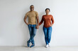 © Anastasiya - A smiling black couple holding hands and smiling at camera while standing against white studio wall, african american man and woman in casual jeans and t-shirts posing together, copy space