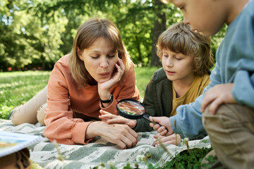 Wall Mural - Portrait of happy family lying on picnic blanket in park together and using magnifying glass exploring nature looking at little bugs