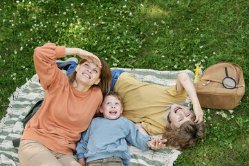 Wall Mural - High angle portrait of family lying on blanket in park and looking up with smiles looking at clouds and daydreaming copy space