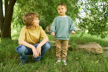 Wall Mural - Two brothers spending time together in green park outdoors with older boy watching baby brother with love and affection