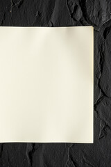 Poster - Blank white paper sheet lays on dark stone surface. Simple image of plain document on rough textured background. Contrast of materials. Clean empty space for message or art.