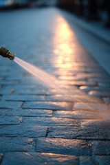 Poster - sweeping motion of water from hose cleaning cobblestone street creating reflections under soft light