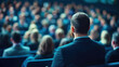 © Ivan - Attendees are seated and focused on a presenter at a conference. The environment is lively with a professional atmosphere and engaged participants