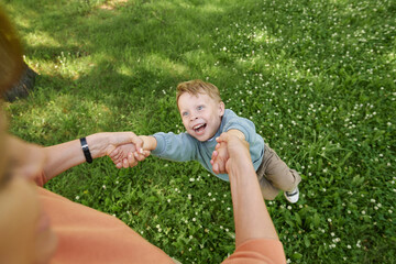 Wall Mural - POV of mother holding hand with little boy and spinning playing together in green park outdoors copy space