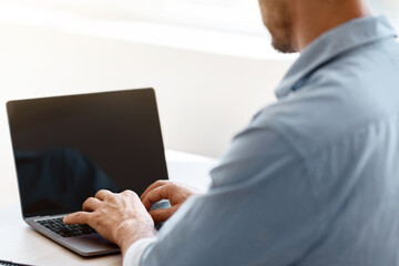 Poster - Unrecognizable businessman working on laptop with black screen, sitting at desk in office, typing on keyboard, answering emails, browsing new website, over shoulder view, mockup image with copy space