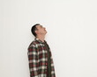© Oleksandr Zinchenko - A man stands in an indoor area, looking up thoughtfully at a blank white wall. The space is bright, highlighting his casual outfit of a plaid shirt over a t-shirt, creating a serene atmosphere