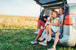 © Soloviova Liudmyla - Portrait of Happy young couple with little daughters sitting inside car trunk during auto trop. They are smiling, laughing and chatting. Family values, traveling concept.