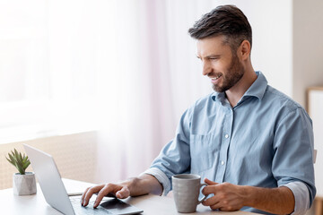 Poster - Home Office. Smiling Freelancer Man Checking Emails On Laptop And Drinking Coffee, Enjoying Working Remotely, Copy Space