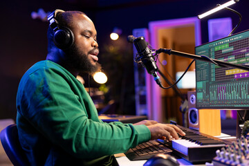 Leinwandbilder - Young artist playing piano keys and singing song on microphone, composing his new music and mixing the tracks on digital interface. Producer technician composing melody with gear.