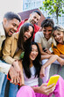 © Xavier Lorenzo - Young happy group of diverse friends laughing while using mobile phone at city street, enjoying social media content