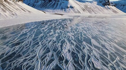 Wall Mural - aerial pan over frozen river patterns amidst snowy mountains in winter landscape
