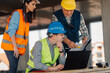 © Ljustina - Construction engineers reviewing blueprints on building site using laptop