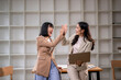 © Apichat - Two women are high fiving each other in a business setting