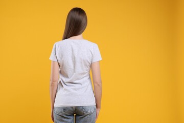 Wall Mural - woman wearing blank white t-shirt on orange background, back view. mockup for design