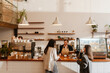 © Drobot Dean - A White, overweight female barista aged 25, taking the order from two women in their late 20s, with a wide smile on her face, as she stands behind the counter in a cozy coffee shop