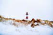 © Connect Images - A red and white lighthouse stands amid snow-covered dunes under a bright sky. Sylt, Germany