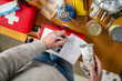 © Connect Images - Person makes list of emergency supplies on wooden table with canned goods and red first aid kit. Preparing a survival weekend